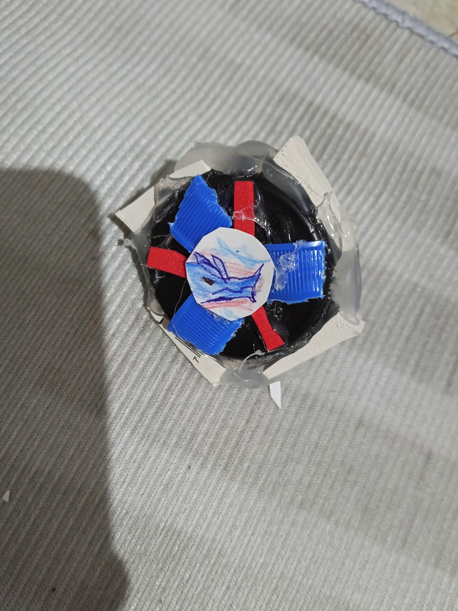 Colar a tampa grande (a laranja q apareceu no vídeo) nas outras peças,colar a borracha,Eva,pedaços da garrafa e o desenho no topo 