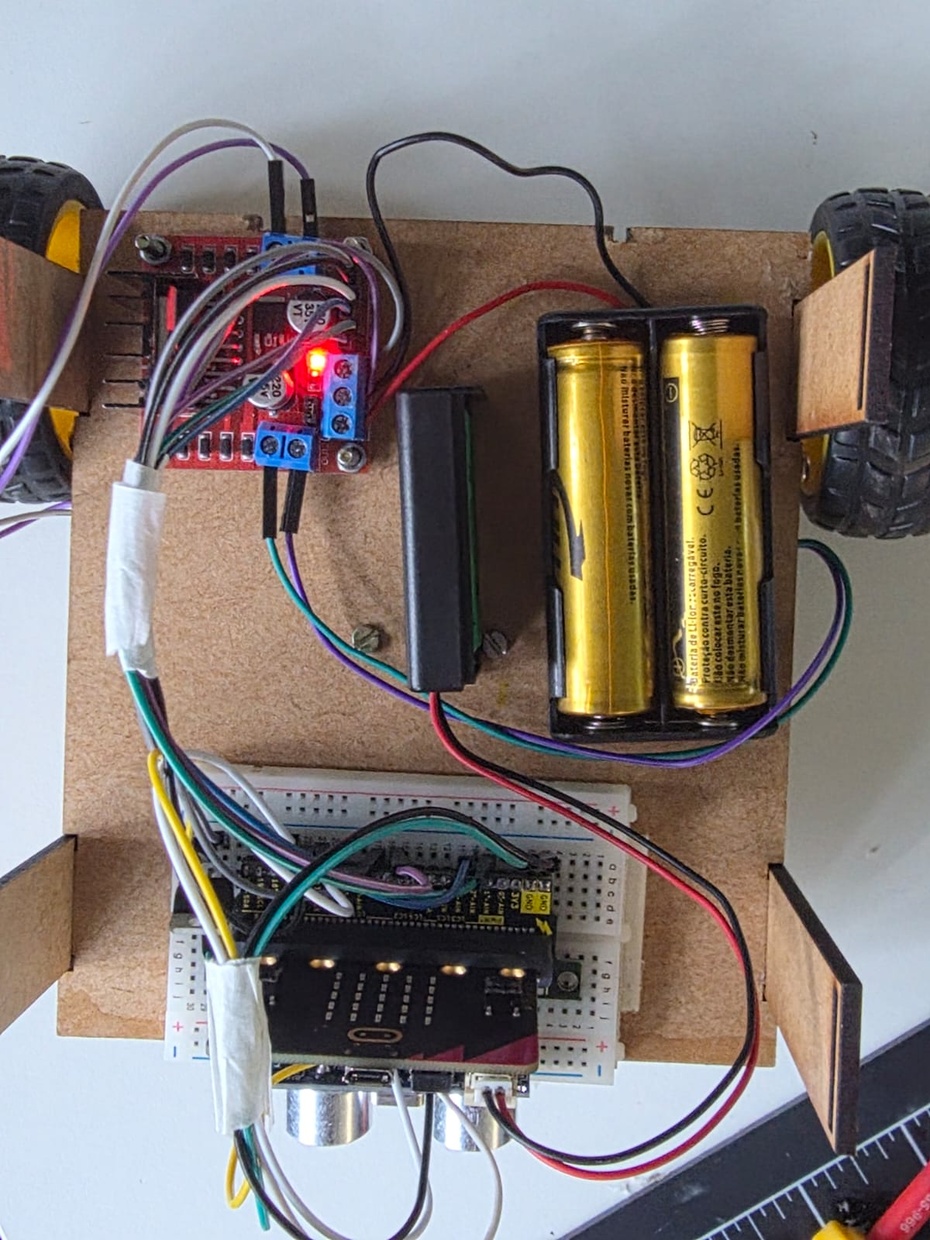 Adição das pilhas ao circuito

Antes de incorporar as pilhas ao circuito, é importante destacar que, ao conectar o circuito ao computador para inserir a programação no micro:bit, deve-se, antes, desconectar as pilhas de seus suportes. Além disso, lembre-se, sempre, de colocar a parte lisa da pilha junto da mola e, nunca, a parte não lisa, evitando um curto-circuito e a queima de componentes eletrônicos. Nesse sentido, para adição das pilhas ao circuito, deve-se seguir os próximos passos:
- Conectar um dos fios (no caso da imagem acima, o fio preto) do suporte de pilhas da ponte-H na entrada GND da ponte-H;
- Conectar um dos fios (no caso da imagem acima, o fio vermelho) do suporte de pilhas da ponte-H na entrada 12V da ponte-H;
- Conectar o conjunto de fios vermelho e preto do suporte pilhas na entrada localizada na parte superior do micro:bit.