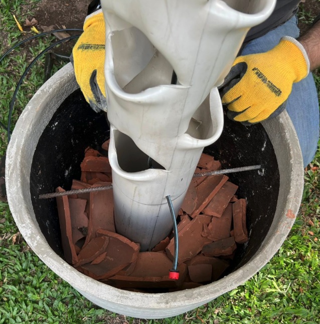 Posicione o cano no centro do vaso e crie uma primeira camada dom cacos de tijolo. Não esqueça de fazer isso dentro e ao redor do cano.
