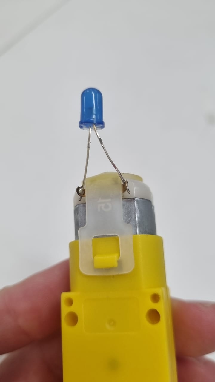 Solde os terminais do led, um em cada terminal do motor. Não tem jeito certo ou errado de soldar aqui, inverter a polaridade do led apenas muda o sentido que você precisa girar a manopla para ele acender.