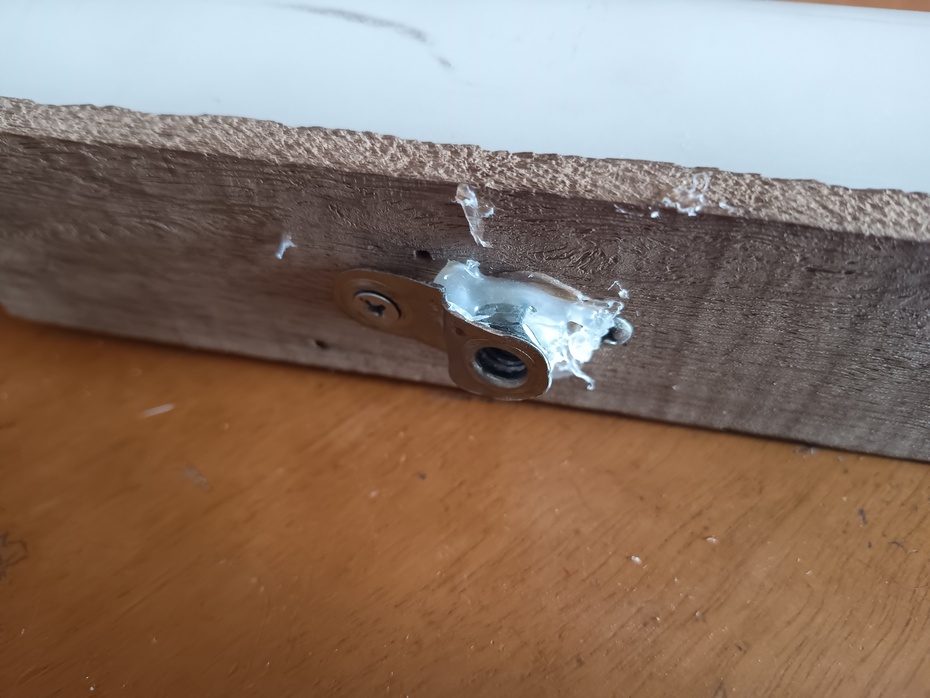 Coloque a porca no meio da ripa e cole as bordas da porca na ripa com cola-quente, em seguida, amace a cantoneira até ela formar um "_Γ", em que um dos furos deve estar sobre e rente o furo da porca, no outro furo, marque e faça um buraco de 2mm e parafuse a cantoneira nessa posição.