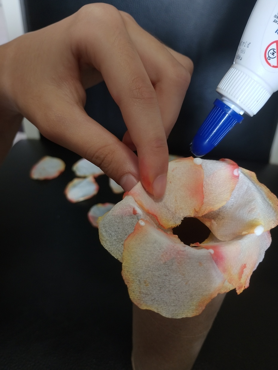Coloque as pétalas uma sobrepondo a pontinha da outra na borda da parte de cima do tubo de papelão e vá colocando a cola líquida entre uma pétala e outra sempre no mesmo sentido e reserve uma pétala para próxima etapa.