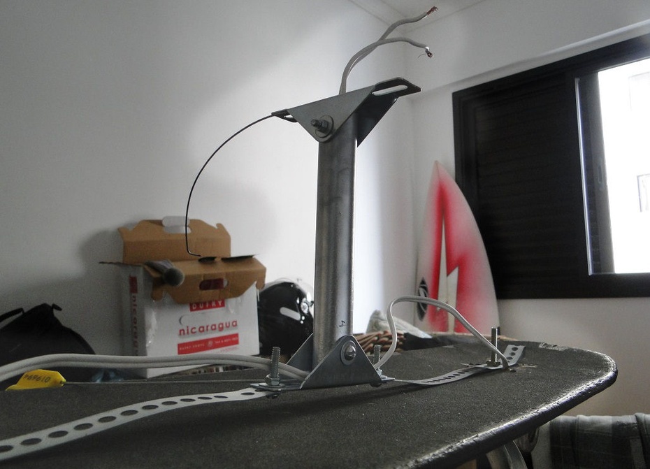 Aqui é onde pode complicar um pouco. Mas com a imagem, vou conseguir explicar: Tem esses dois triângulos de ferro, um vai no teto, o outro na fita metálica perfurada e ambos conectados no tubo de PVC de 20cm (pintado na cor de sua preferência). O shape precisa de dois furos em cada posição de cada truck. Os fios de cada truck passa por um dos furos do shape e o outro furo vai o parafuso grande, que passa pelo "T", passa pelo shape e aproveita para já passar por um dos furos da fita metálica perfurada (igual a imagem). Os dois fios que vem dos dois trucks passam por dentro do tubo de PVC e vai até o teto para ligação na rede elétrica.