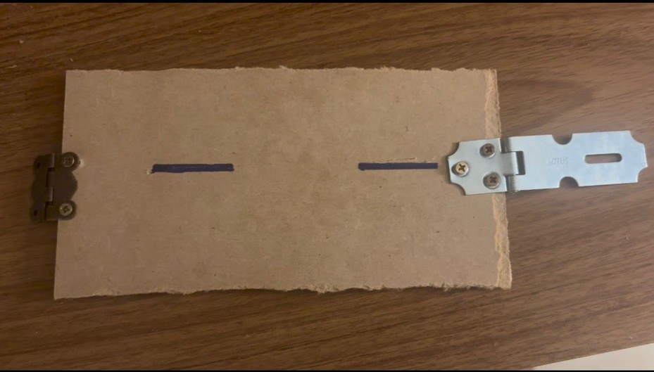 Use uma parte de 20 cm x 10 cm para ser a tampa superior, faça as marcações dos furos para entrada de dinheiro e fixe a dobradiça e o trinco usando parafusos, conforme figura.