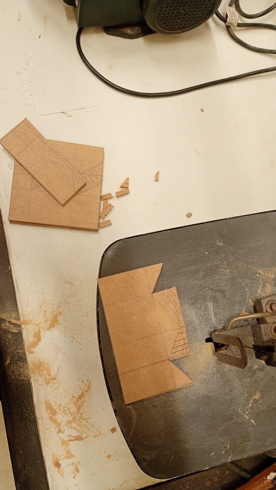 Com os quadrados maiores cortados, use a serra tico-tico para fazer os cortes menores no formato dos dentes conforme o desenho técnico. Tenha as mãos firmes e corte devagar seguindo o traçado para garantir precisão e evite lascas. 

Após realizar os cortes dos dentes, utilize a serra copo de 35 mm para fazer o furo central em uma das placas de 114 × 108 mm. 

Em seguida, use a serra copo de 16 mm para criar os formatos dos olhos nas placas de 120 × 120 mm, conforme indicado no desenho técnico.