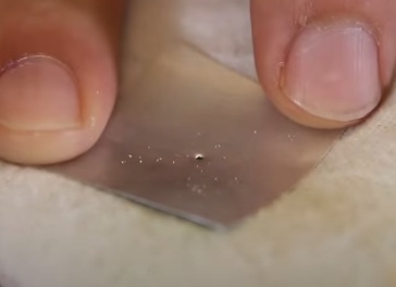 Com uma agulha faça um furo bem no centro do pedaço de alumínio. Este furo precisa ser bem pequeno então faça com cuidado. Para facilitar, coloque um tecido qualquer dobrado por baixo da peça e então pressione a agulha contra o alumínio.