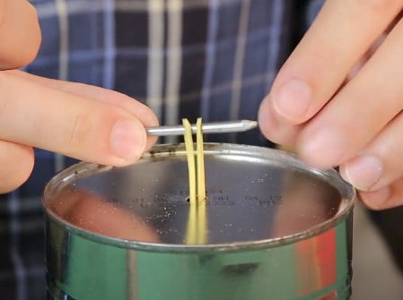 Passe um dos lados de cada elástico ,de dentro para fora, pelo furo feito no fundo da lata, passe um prego por dentro dos elásticos e encostando o prego na lata pelo lado de fora o fixe com fita adesiva na base da lata.