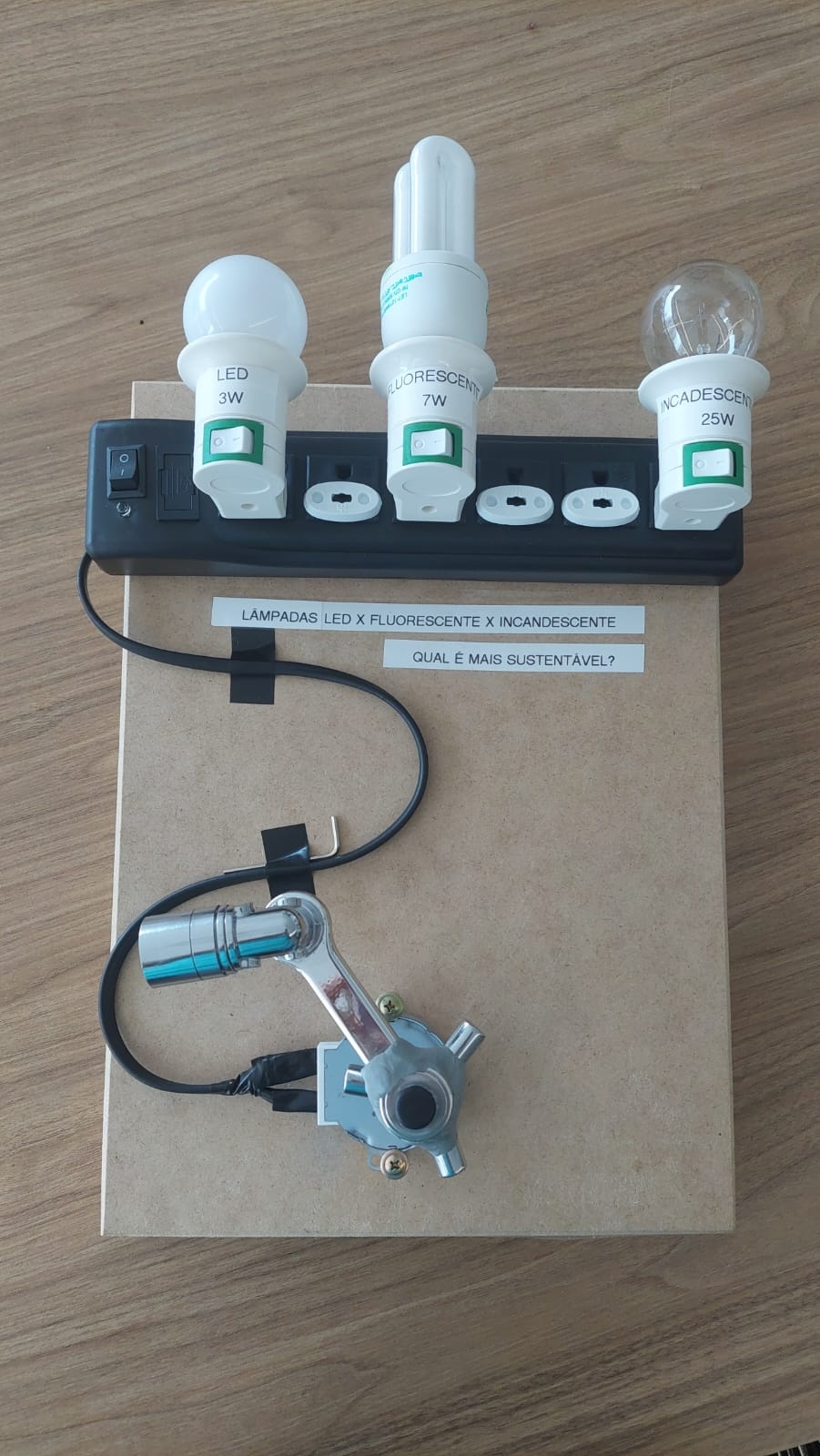 1º- Em uma base de MDF, colei com fita dupla face um filtro de linha;
2º- Cortei o fio do filtro de linha e liguei aos conectores do motor de prato de micro-ondas através de conectores elétricos e isolei com fita isolante;
3º- Colei o motor na base de MDF com fita dupla face e parafusei-o na base com 2 parafusos para maior segurança, também prendi o fio do filtro de linha na base;
4º- Pluguei 3 soquetes de lâmpadas com interruptores no filtro de linha e isolei as demais tomadas que não seriam usadas com protetores de tomadas;
5º- No primeiro soquete coloquei uma lâmpada de LED de 3W, no segundo soquete coloquei uma lâmpada Fluorescente de 7W e no terceiro soquete coloquei uma lâmpada incandescente de 25W que são equivalentes.
6º- Acoplei ao pino do motor de prato de micro-ondas um volante de metal para registro hidráulico modelo cruzeta e apertei com a chave Allen.
7º- Acoplei ao volante cruzeta, com durepoxi, um extensor de torneira giratório, que funcionou como minha manivela.