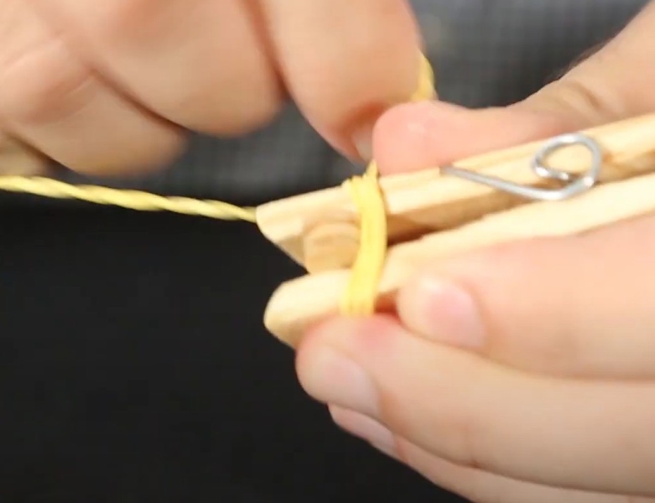 Usando um elástico em uma ponta do retângulo enrole e prenda, cruzando em formato de “X”, o conjunto de palitos e prendedor de roupas.